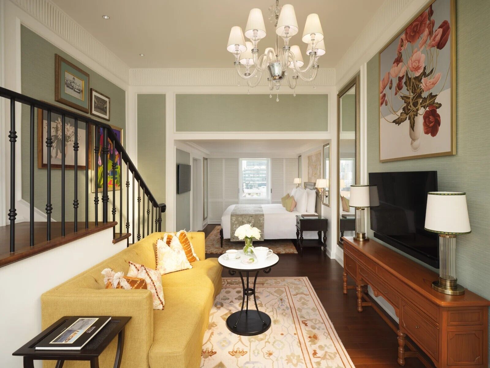 A hotel room with a sofa, a small round table, a TV, a chandelier, and a painting.