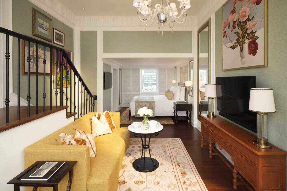 A hotel room with a sofa, a small round table, a TV, a chandelier, and a painting.