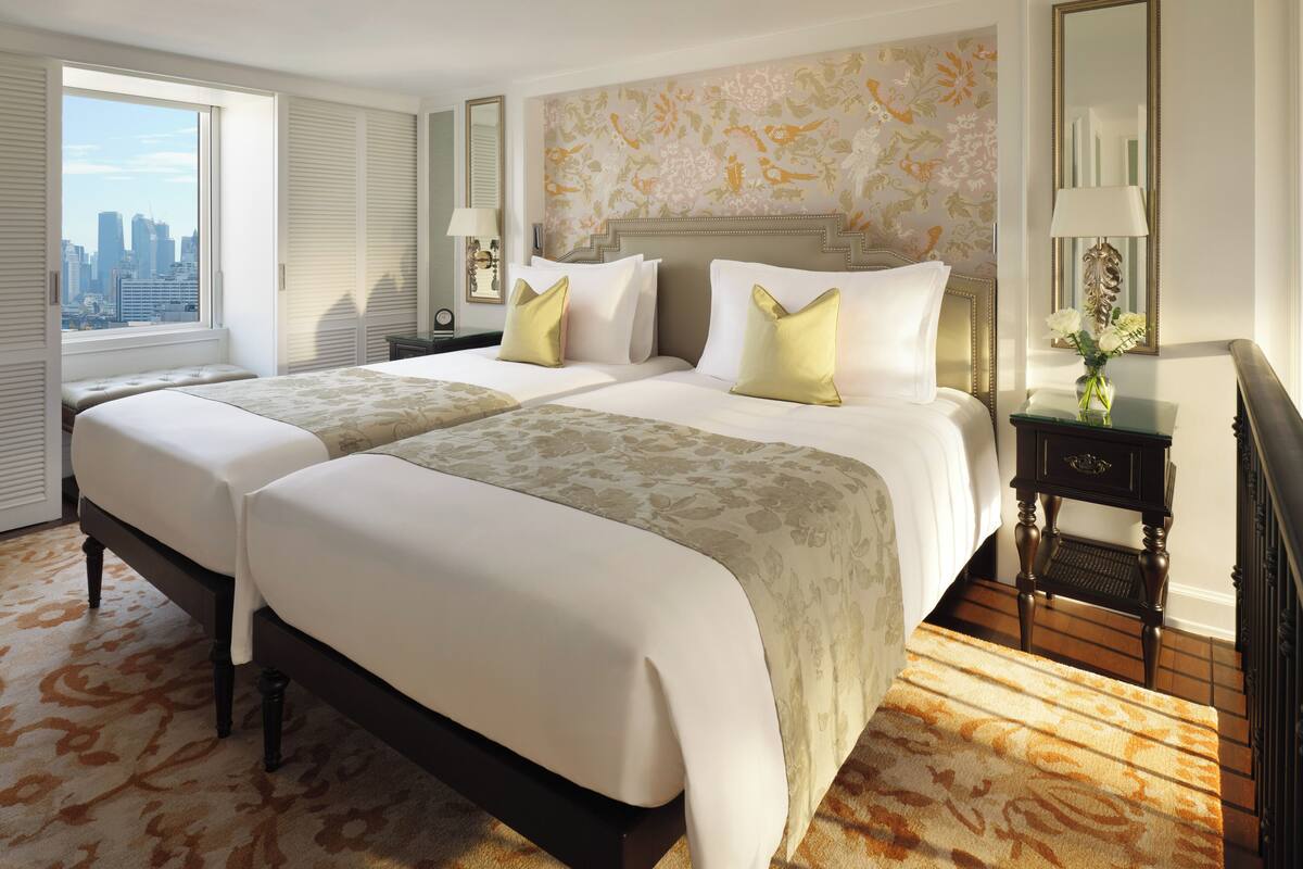 Habitación de hotel con dos camas, vista a la ciudad, alfombra estampada y un espejo decorativo.