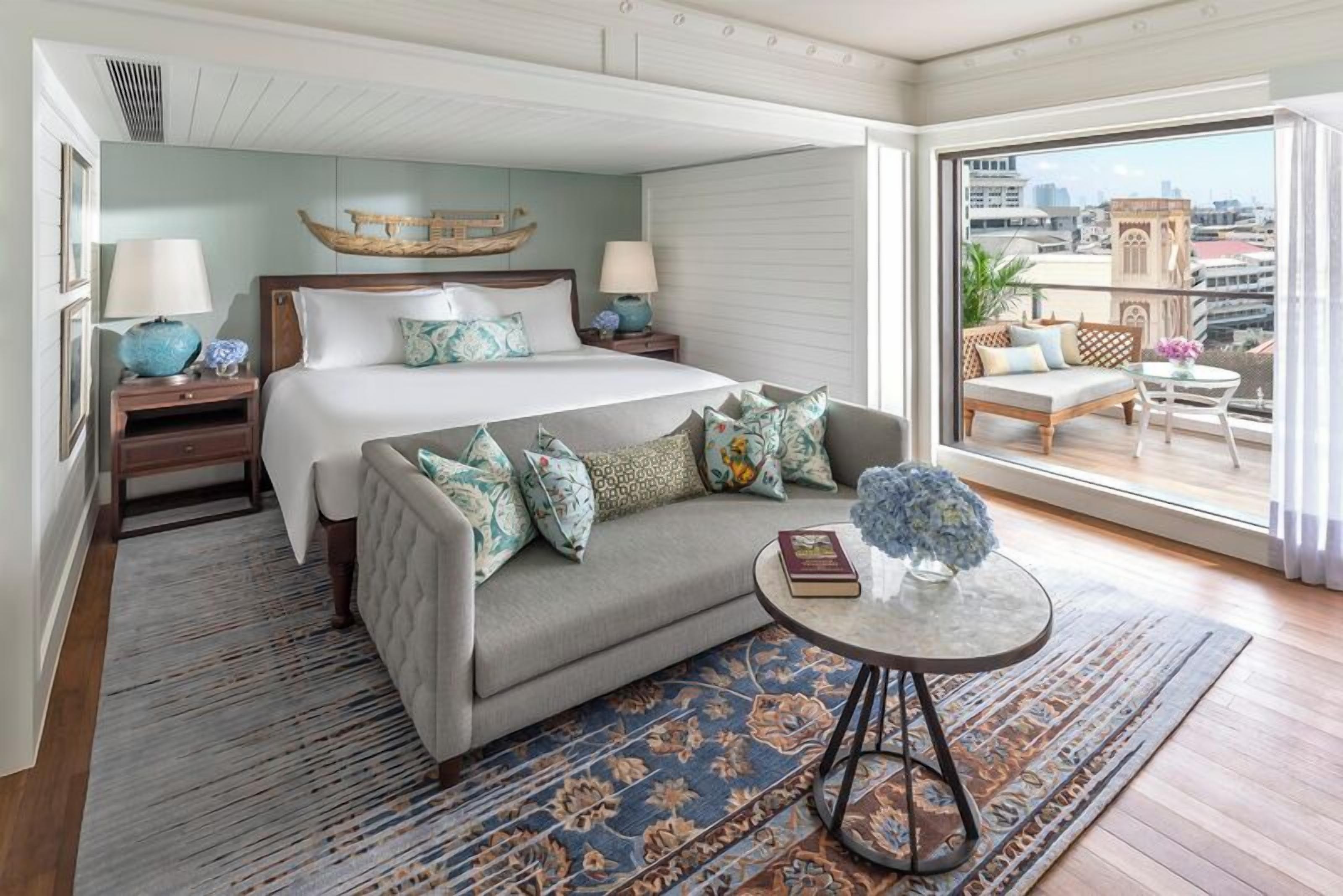 A bedroom with a bed, a sofa, a small table, and a balcony with a view of the city.
