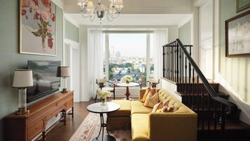 A spacious living room with a large window, a chandelier, a sofa, a television, and a wooden cabinet.