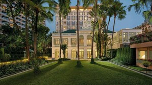 A large hotel with a symmetrical facade, multiple balconies, and a well-maintained garden with palm trees and hedges. - Mandarin Oriental, Bangkok (Bangkok)