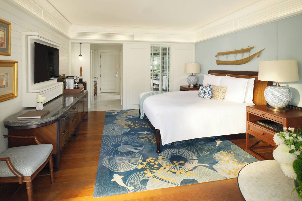 Habitación de hotel con una cama grande, un escritorio con televisor de pantalla plana, un aparador de madera y un ventanal con vistas al exterior.