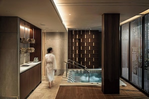 A modern spa area with a hot tub, wooden paneling, and a person in a robe.