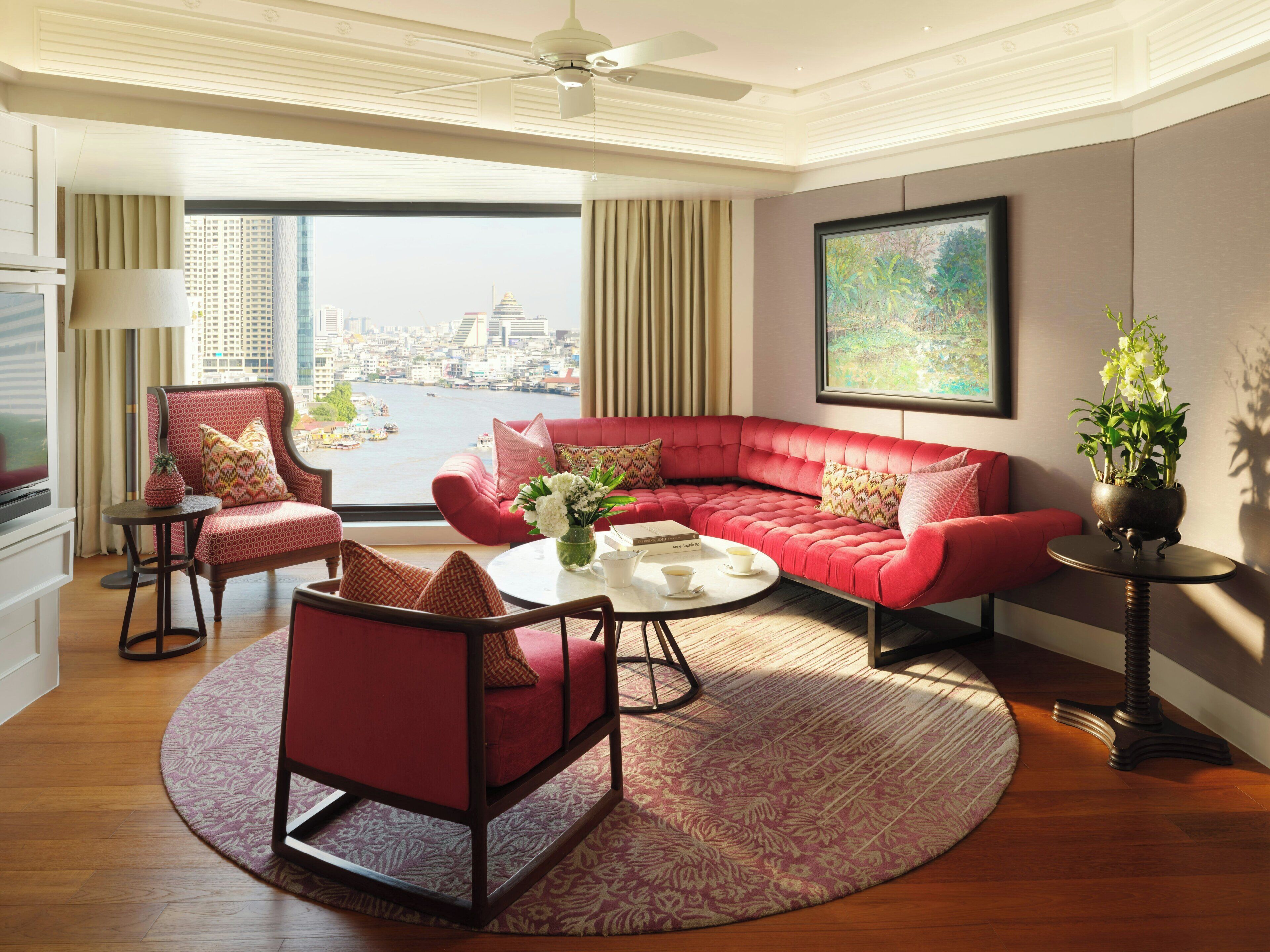 A modern living room with a red sofa, a red armchair, a coffee table, and a view of a cityscape.