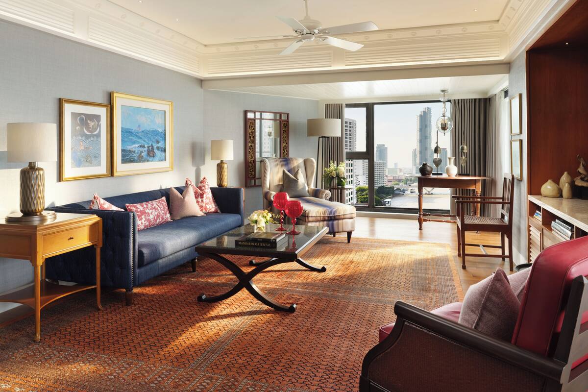Amplia sala de estar con un sofá azul, una mesita de centro y un sillón rojo. Una ventana grande ofrece vistas de la ciudad.