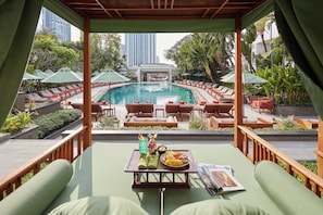 A poolside lounge area with sun loungers and umbrellas, a dining table with a meal, and a view of a swimming pool and high-rise buildings. - Mandarin Oriental, Bangkok (Bangkok)