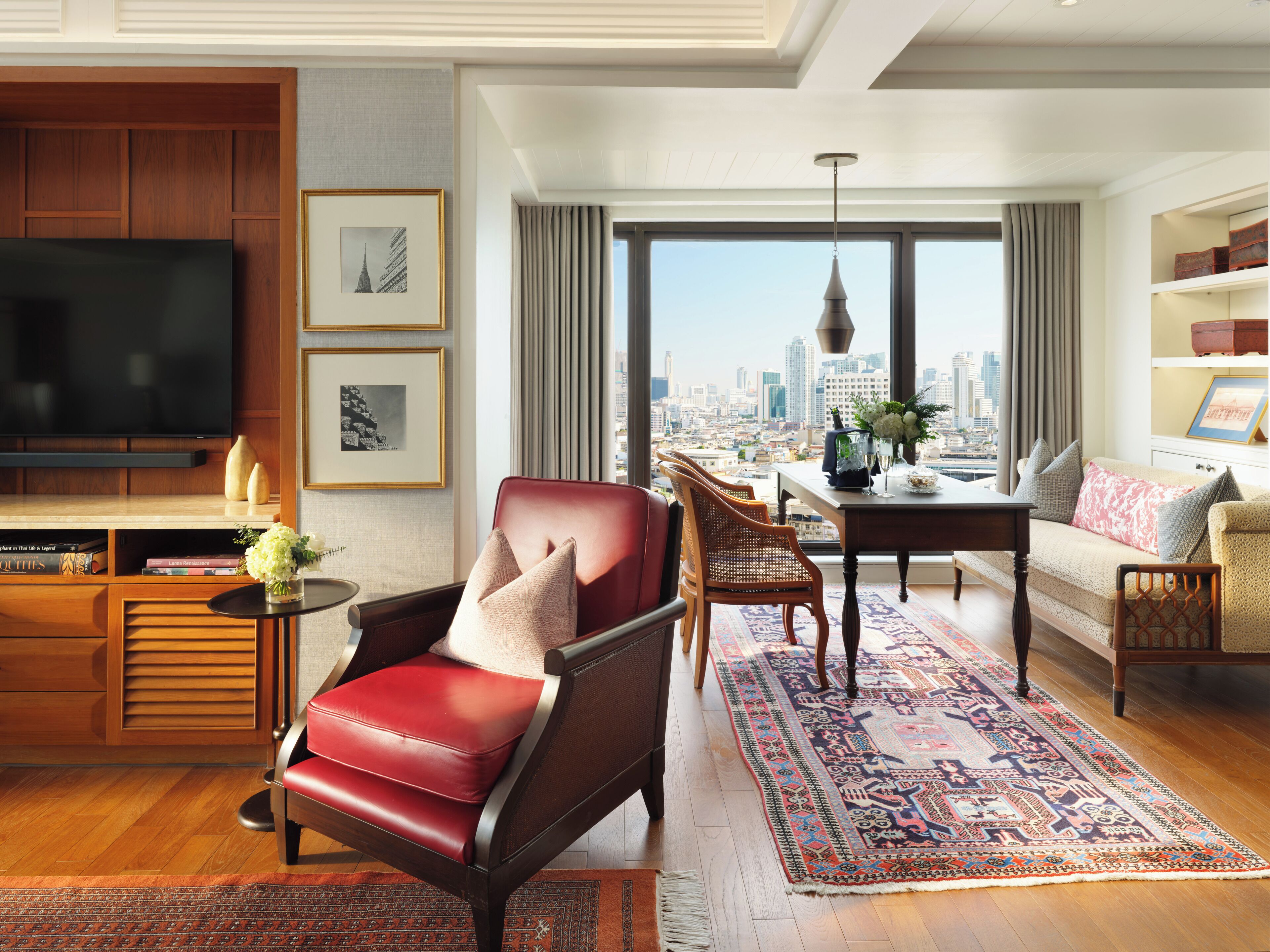 A spacious living room with a large TV, comfortable seating, a dining area, and a city view.