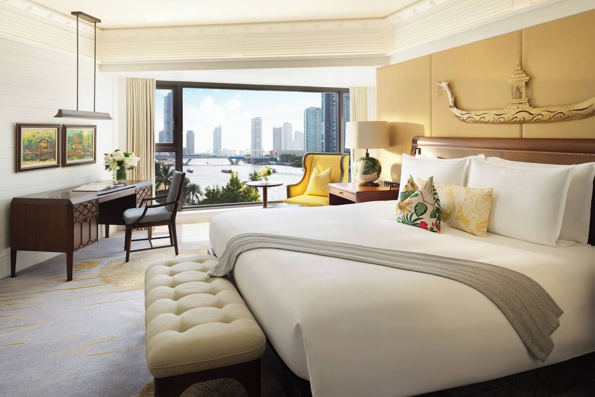 Habitación de hotel con una cama grande, un escritorio, una silla y vistas a un paisaje urbano a través de un ventanal.