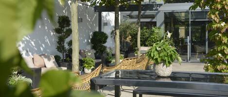 Een terras met rieten meubilair, een glazen tafel en plantenpotten.