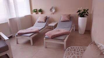 Ein Spa-Behandlungsraum mit zwei Massageliegen, jeweils mit Handtuch und Kopfstütze. Übertöpfe mit Pflanzen und ein dekoratives Wandbild sind ebenfalls vorhanden.