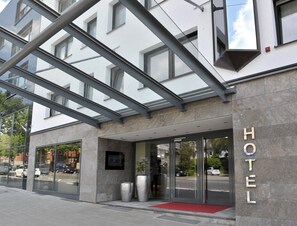Ein Hotelzugang mit Glasfassade, Metallüberdachung und einem roten Teppich, der zur Tür führt.