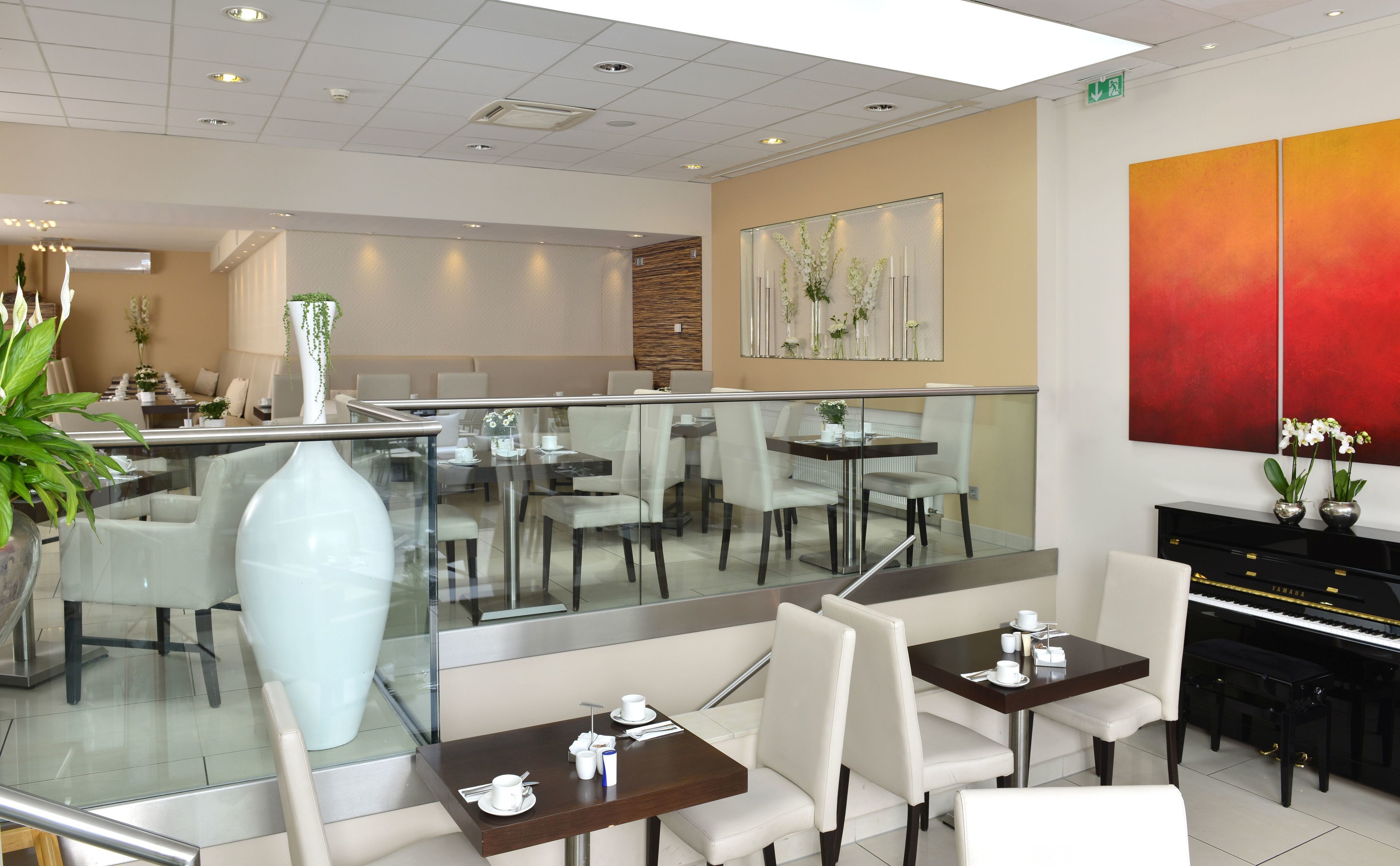 A modern dining area with glass railings, white chairs, and a piano.