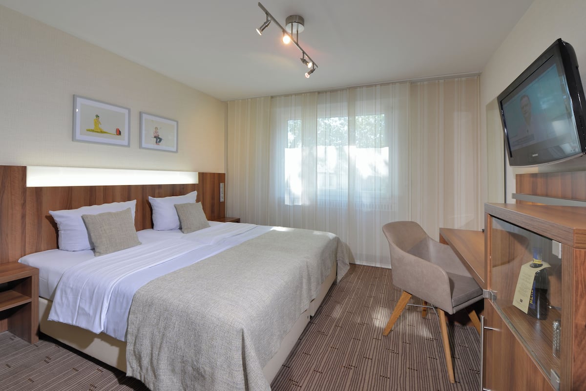 A hotel room with a large bed, a TV, a desk, and two framed pictures on the wall.
