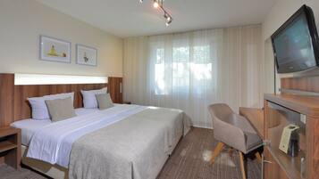 Habitación de hotel con una cama grande, televisión, escritorio y dos cuadros en la pared.