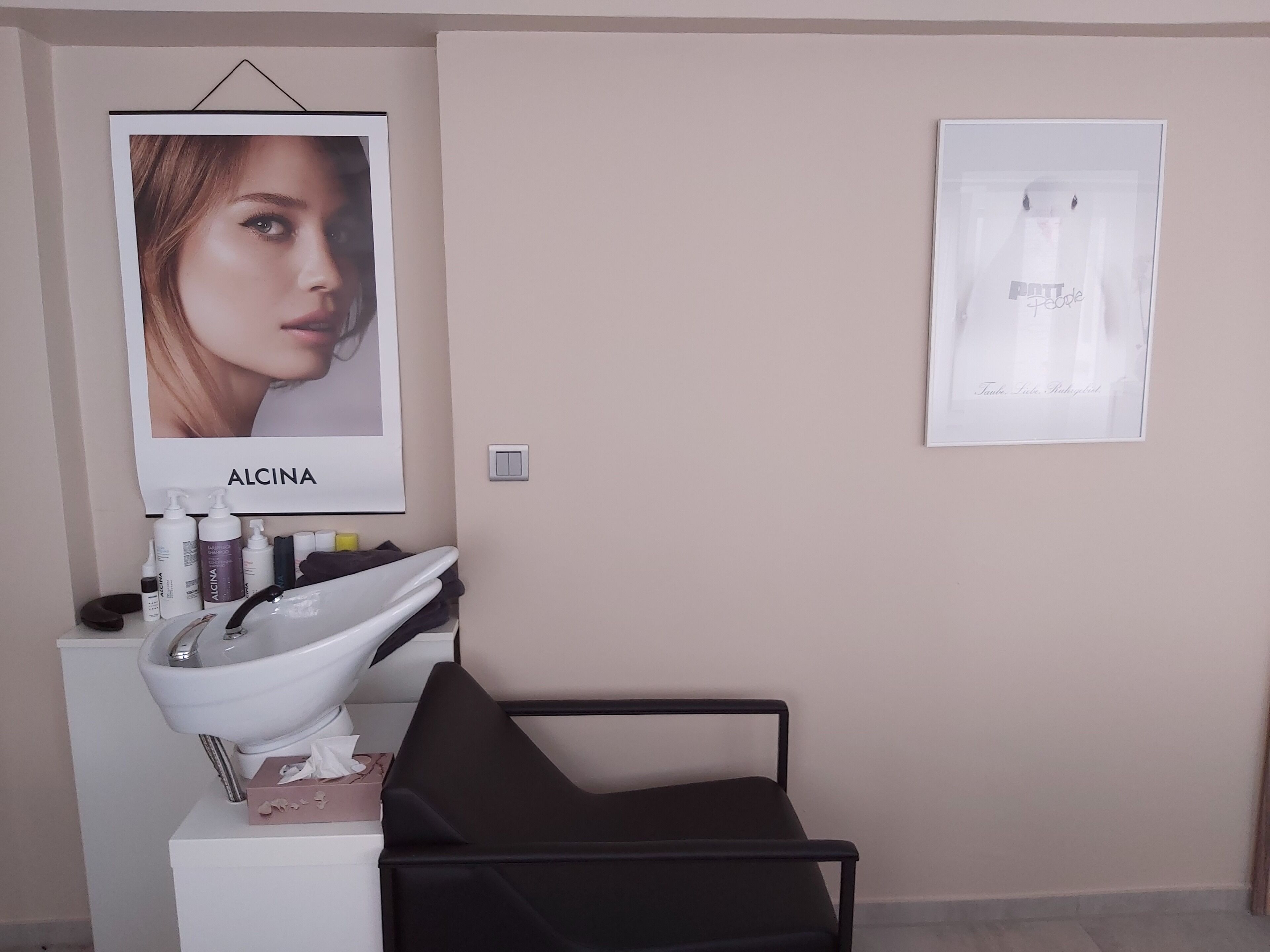 Un baño con un lavamanos blanco, una silla negra y dos carteles enmarcados en la pared.
