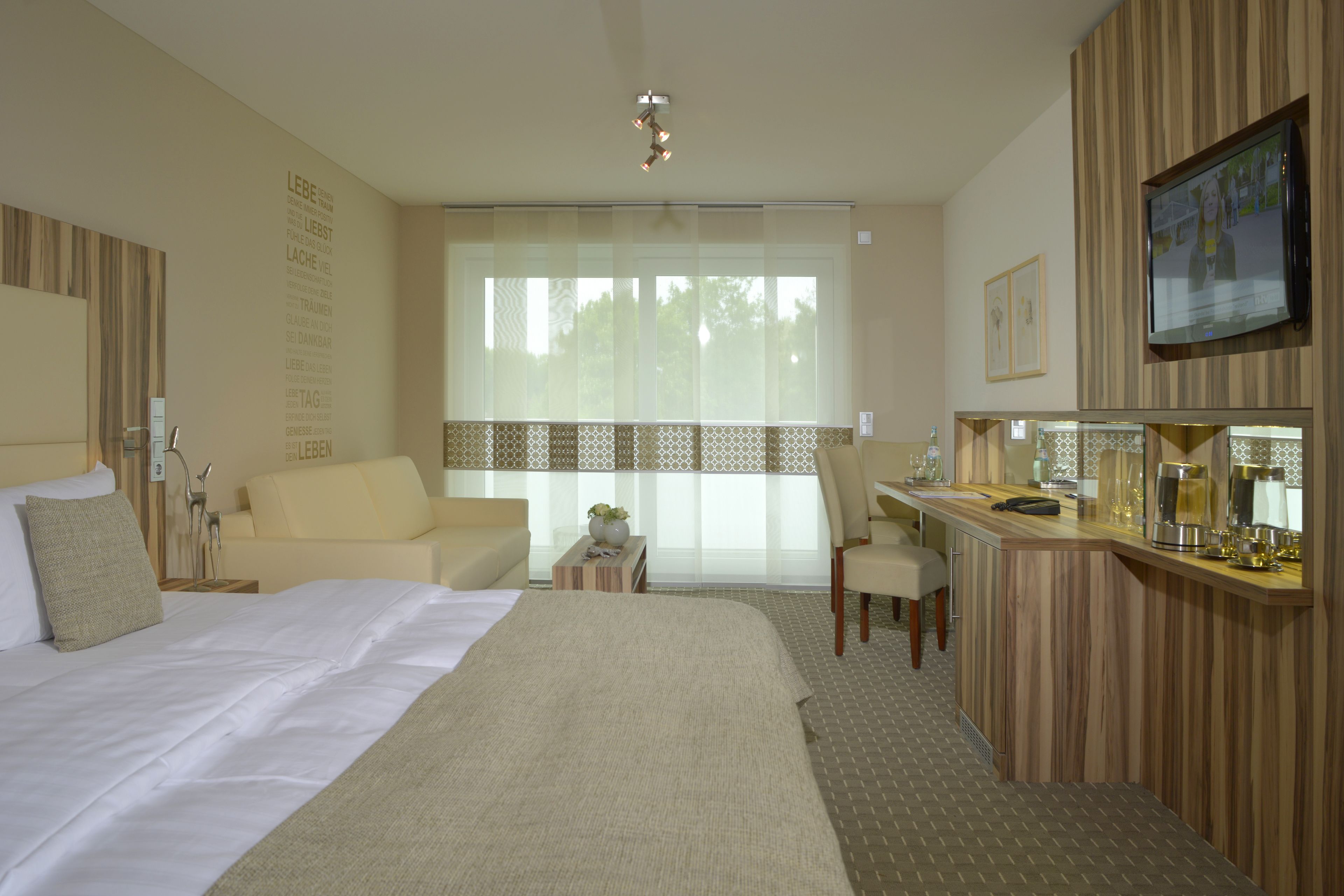 Une chambre d’hôtel avec un grand lit, un bureau, une chaise, une télévision et une fenêtre avec des rideaux légers.