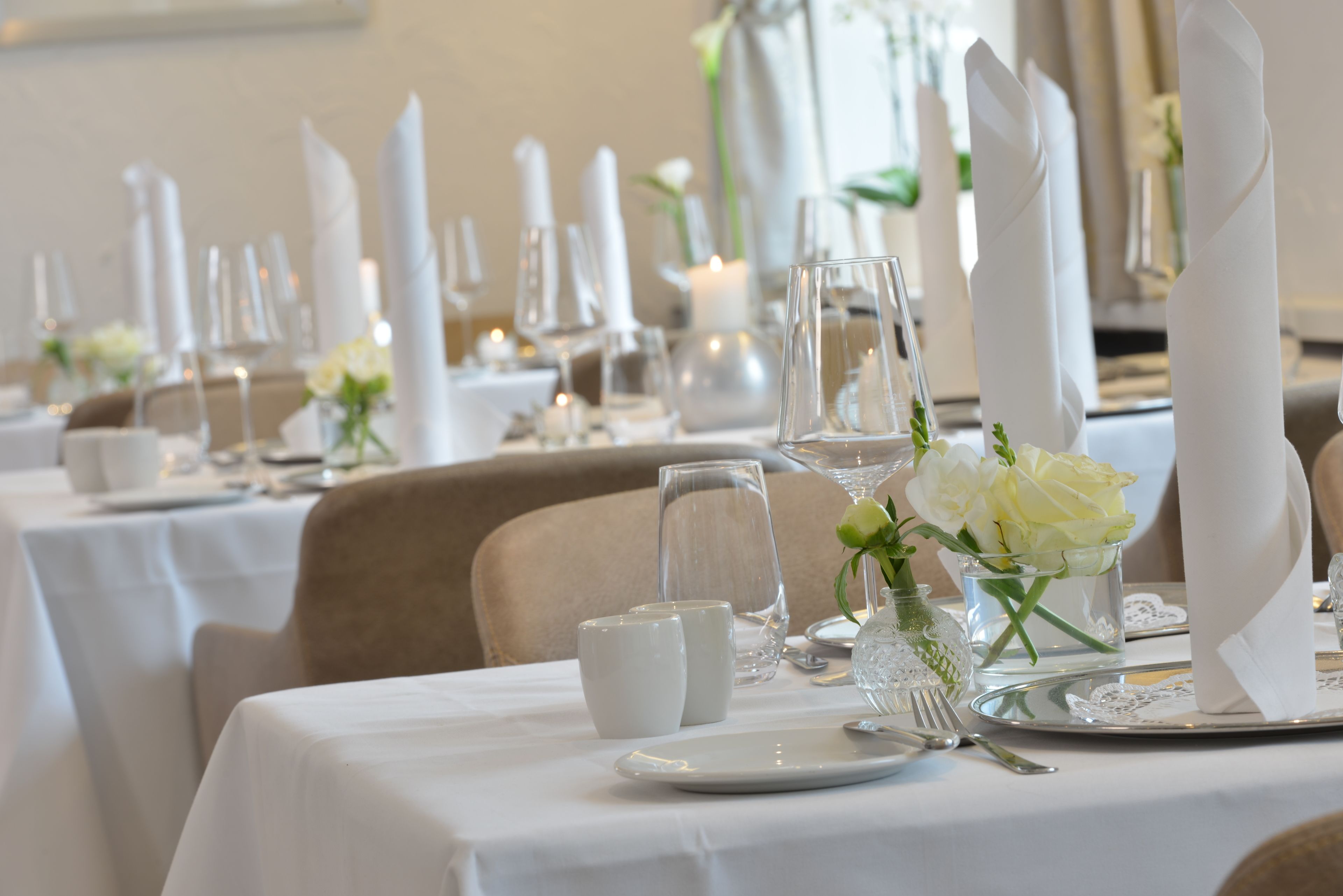 Una mesa de comedor puesta con mantel blanco, cristalería y un florero con flores blancas.