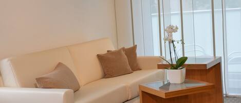 A modern living room with a beige sofa, a wooden side table, and a potted orchid.