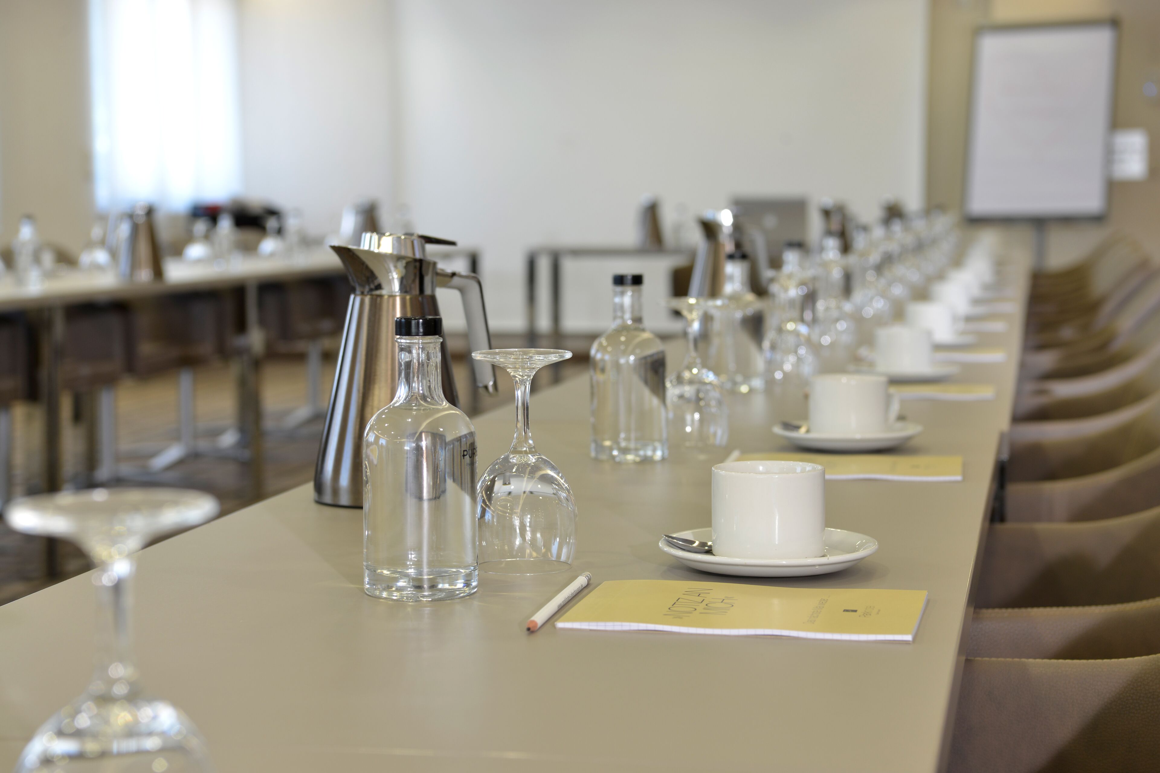 Un salón de conferencias con una larga mesa dispuesta para una reunión, equipado con micrófonos, botellas de agua y tarjetas de identificación.