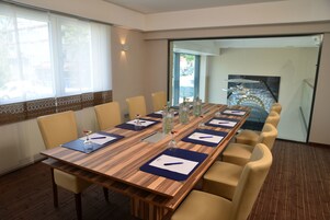 Un salón de conferencias con una larga mesa de madera, sillas color beige y un panel de vidrio.