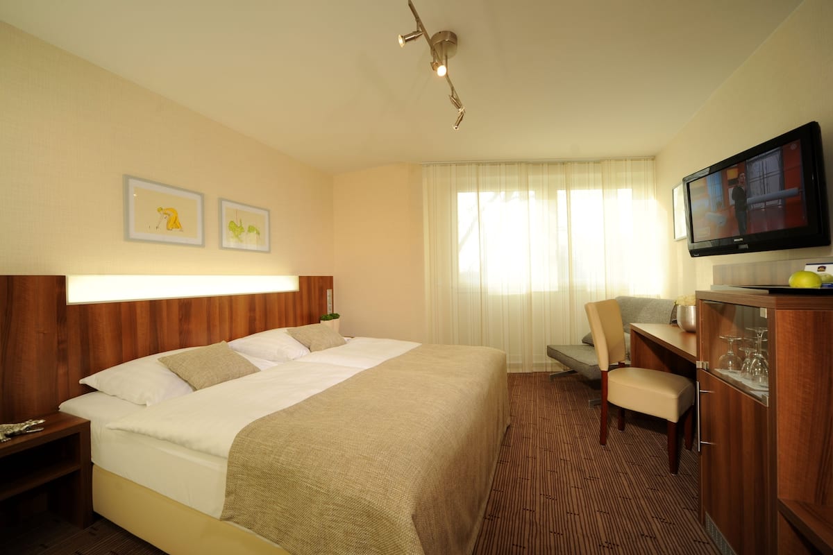 A hotel room with a large bed, a desk, a television, and a window with curtains.