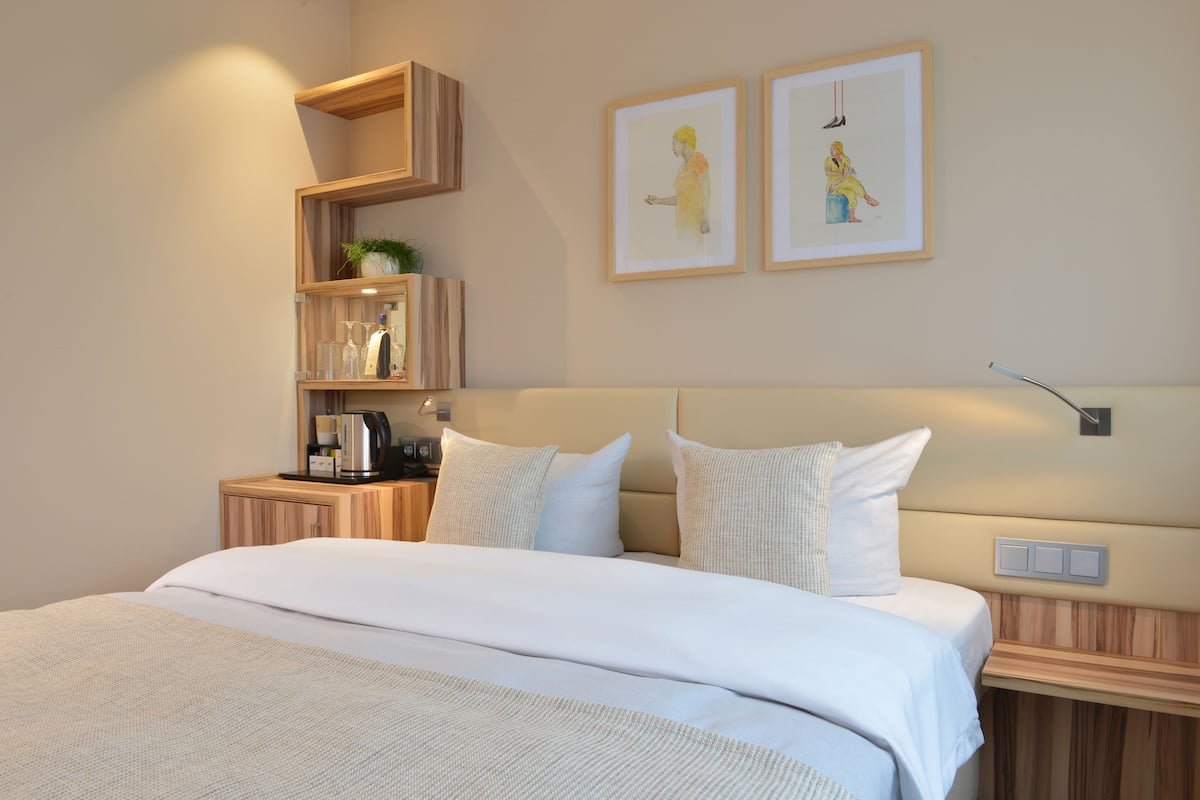 A modern hotel room with a large bed, wooden headboard, bedside tables, and framed artwork on the wall.