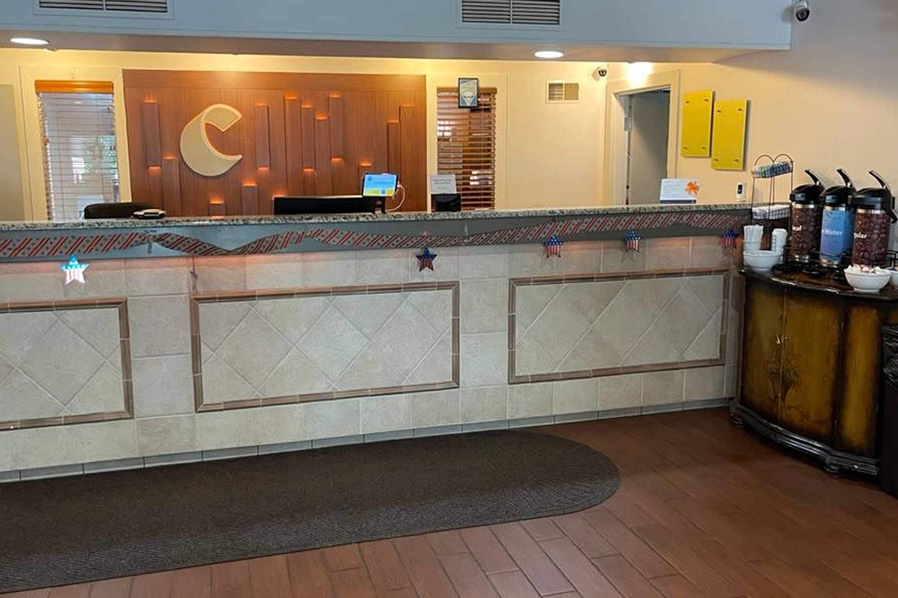 A reception desk with a wooden panel design, a computer monitor, and a coffee station with dispensers.