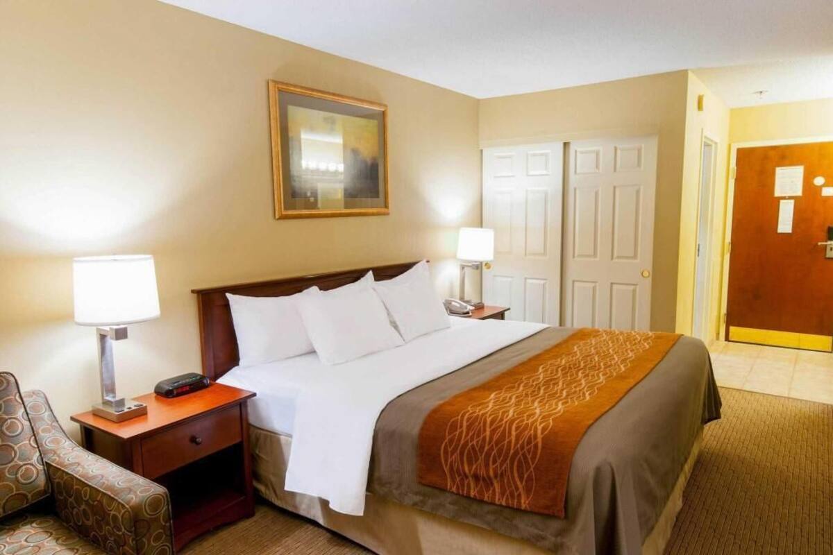 A hotel room with a bed, two bedside tables, a chair, a painting on the wall, and a door.