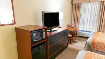 Una habitación de hotel con una cama, un escritorio con computadora, microondas, televisor y ventana con cortinas.