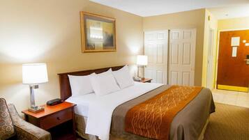 A hotel room with a bed, bedside tables, a chair, a painting on the wall, and a door.