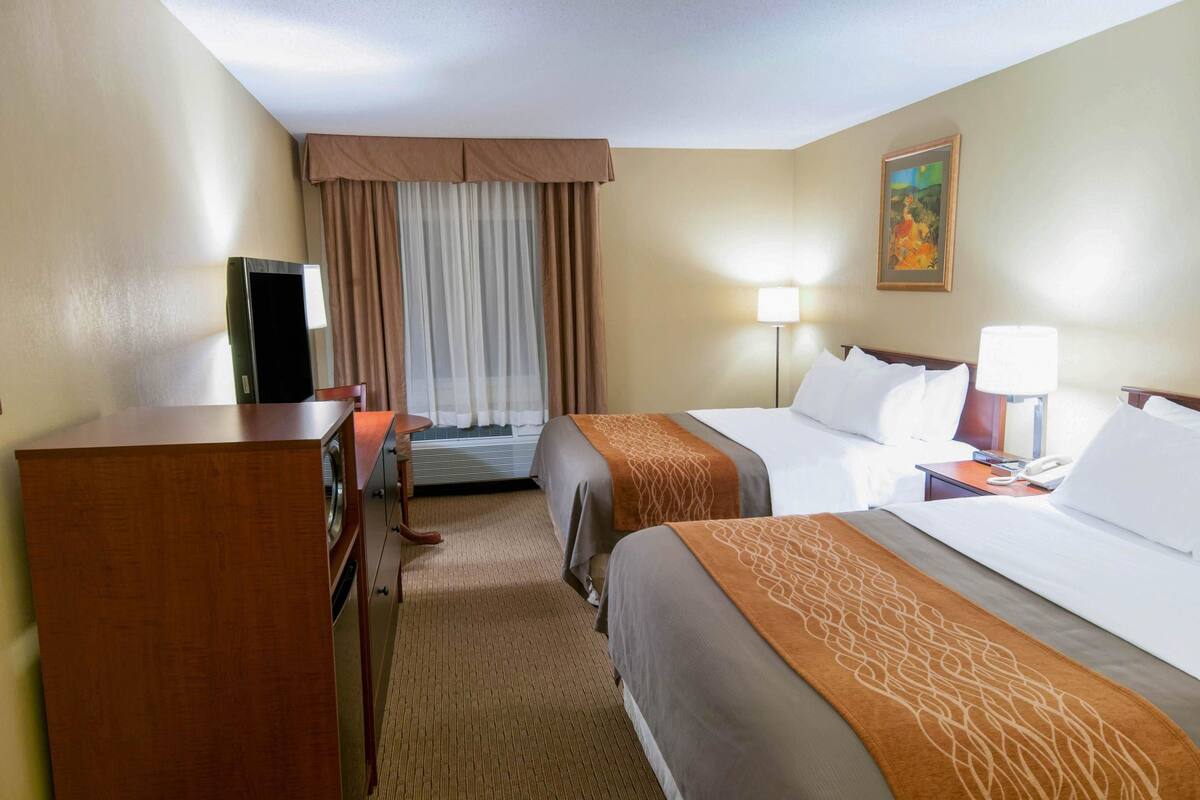 A hotel room with two beds, a desk, a television, and a painting on the wall.