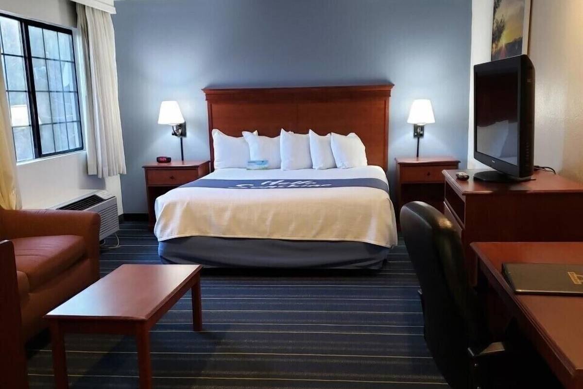 Une chambre d’hôtel comprenant un lit, deux lampes de chevet, une télévision, un bureau, une chaise et une fenêtre avec des rideaux.