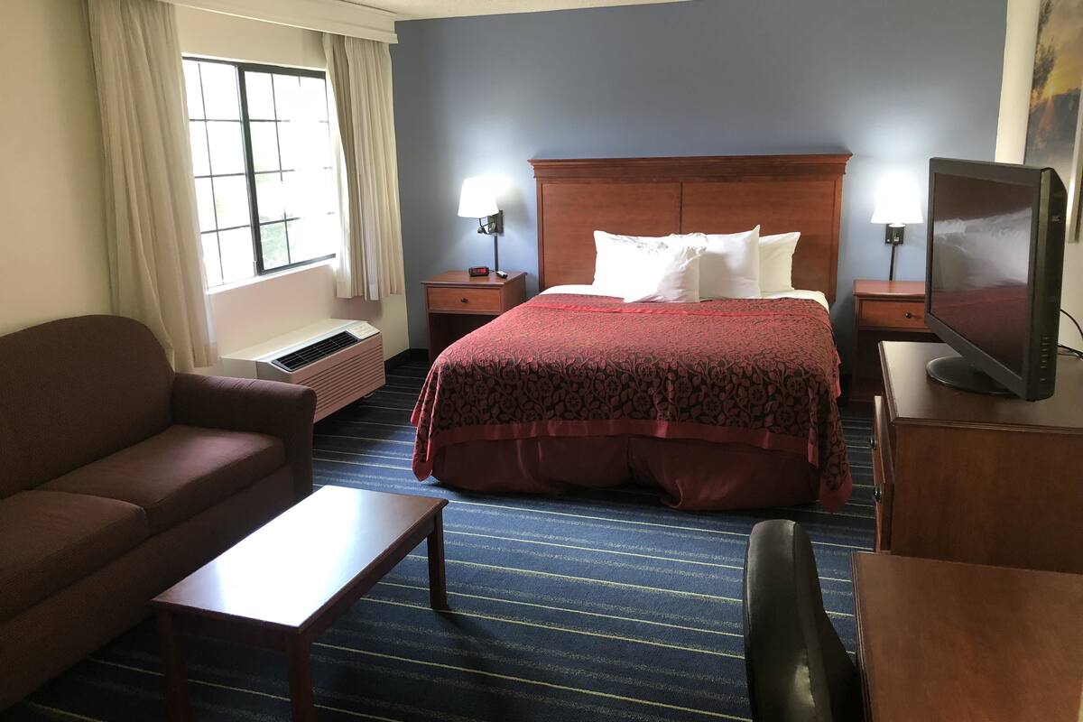 Une chambre d’hôtel avec un lit, un bureau, une chaise, une télévision et une fenêtre avec des rideaux.
