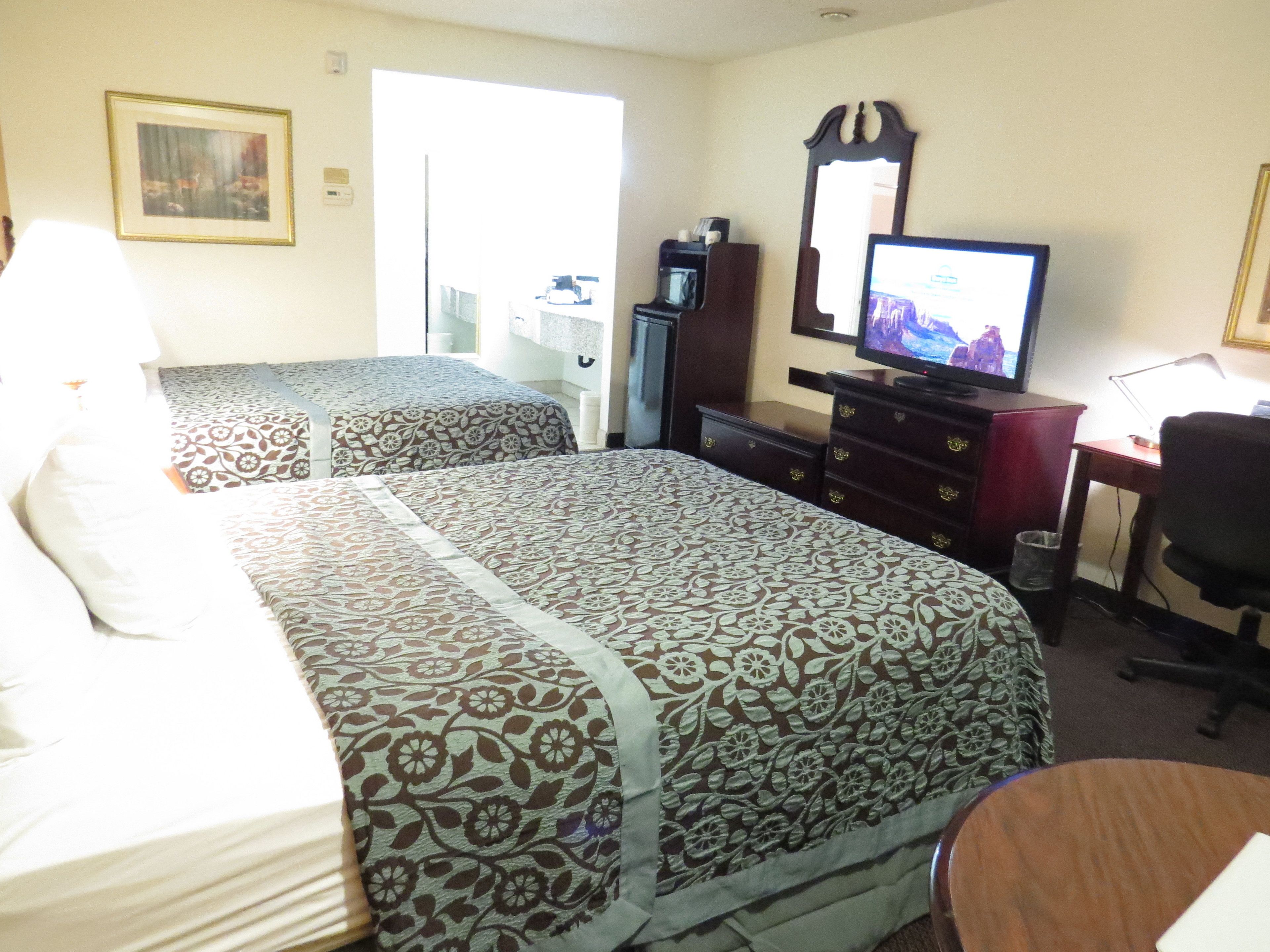 A hotel room with two beds, a TV, a desk with a computer, and a chair.