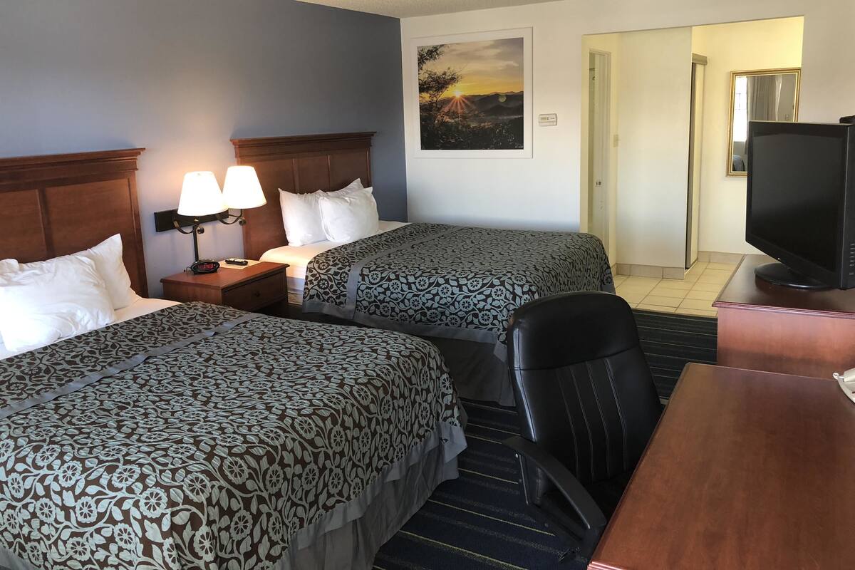 Une chambre d’hôtel avec deux lits, un bureau, une chaise, une télévision et un tableau au mur.