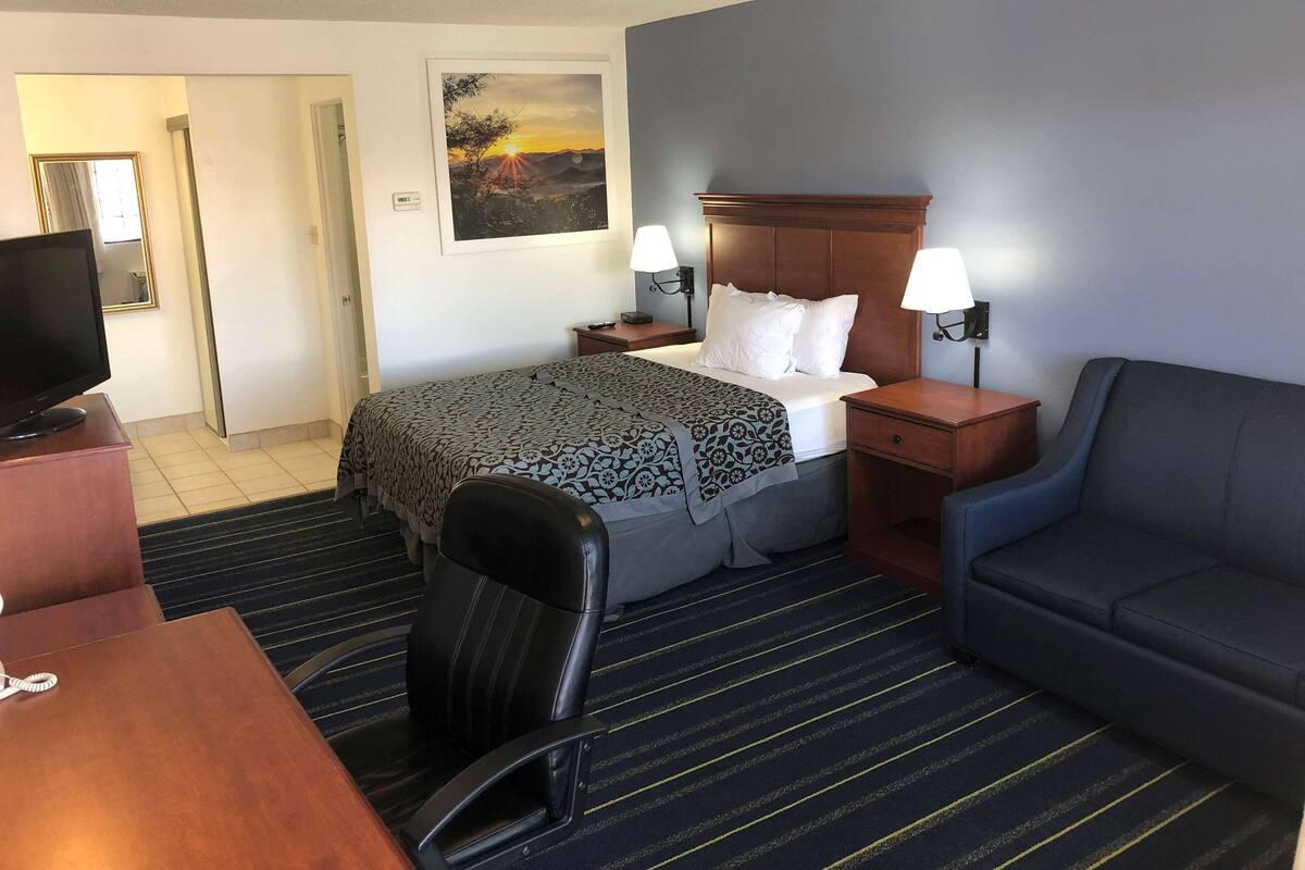 Une chambre d’hôtel comprenant un lit, deux lampes de chevet, un bureau avec une télévision, une chaise et un canapé.