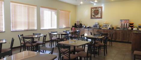 A restaurant with multiple tables and chairs, ceiling fans, and a kitchen area with appliances.