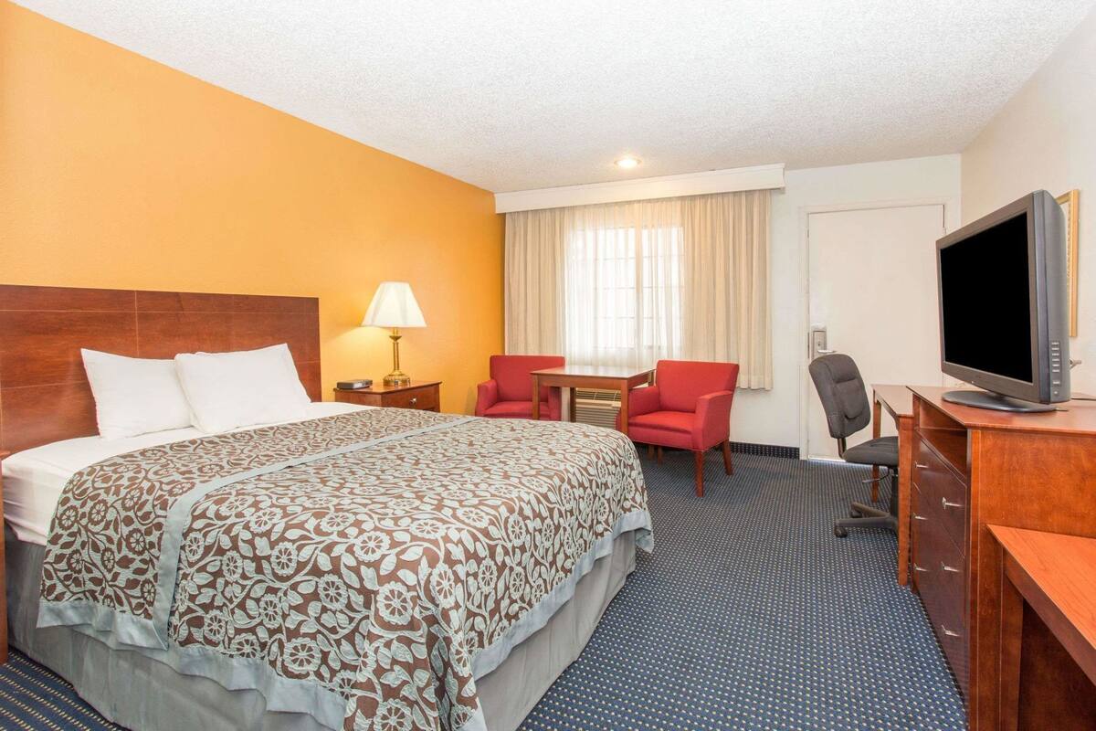 Une chambre d’hôtel avec un grand lit, un bureau avec un ordinateur, une télévision et deux chaises.