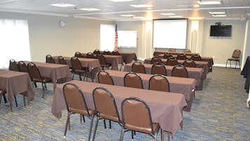 Uma sala de conferências com várias mesas e cadeiras, um relógio na parede e uma tela de projetor.