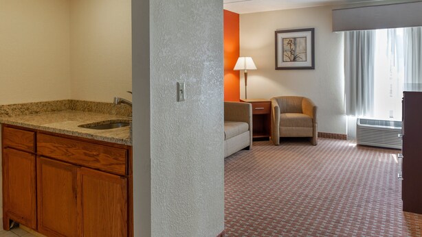 A hotel room with a granite countertop sink, wooden cabinets, a small table with a lamp, a chair, and a framed picture on the wall. - Holiday Inn Express Harrisburg SW - Mechanicsburg by IHG (Mechanicsburg)