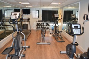 Un gimnasio con varios equipos de ejercicio, incluyendo cintas de correr, elípticas y un estante con mancuernas.
