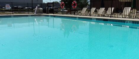 A swimming pool with a black fence, lounge chairs, and lifebuoys.
