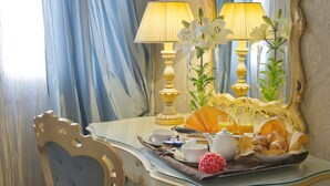 A breakfast tray with pastries, a teapot, and a vase of flowers on a table with a mirror and lamps.