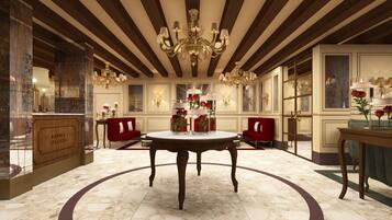 Un hall d’entrée luxueux avec un sol en marbre, une table ronde centrale, des canapés rouges et un lustre.