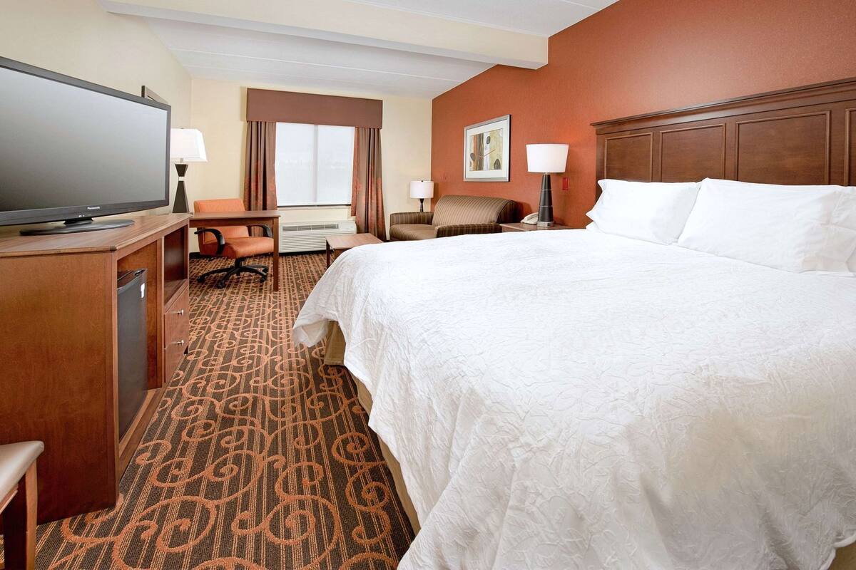A hotel room with a bed, desk, chair, television, and a window with curtains.