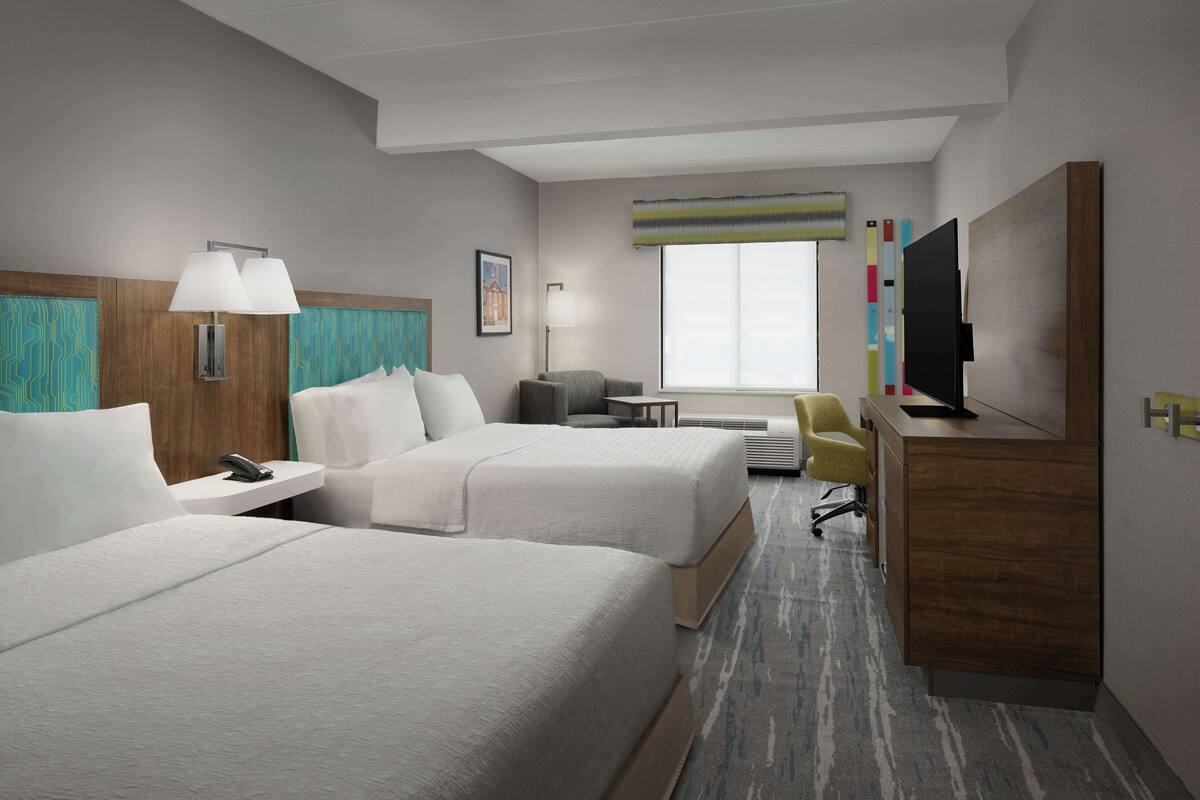 A hotel room with two beds, a desk, a chair, a TV, and a window.
