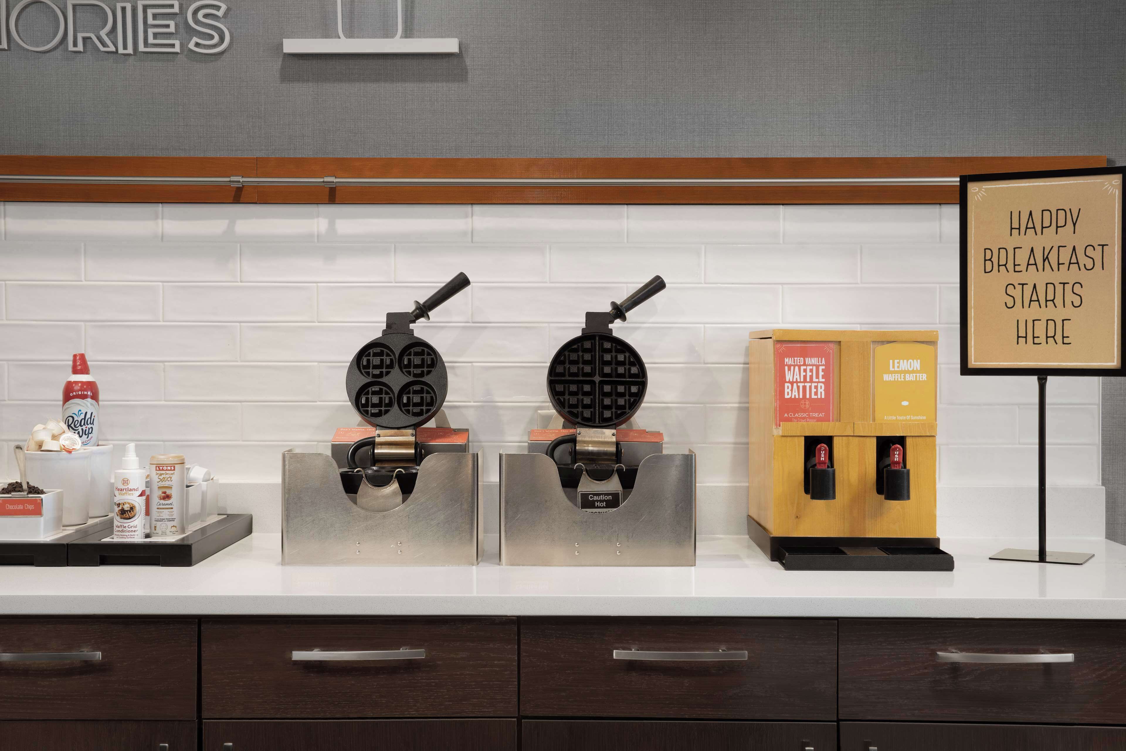 A kitchen counter with waffle makers, a sign that says "HAPPY BREAKFAST STARTS HERE", and a coffee machine.