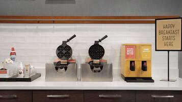 A kitchen counter with waffle makers, a sign that says "HAPPY BREAKFAST STARTS HERE", and a coffee machine.
