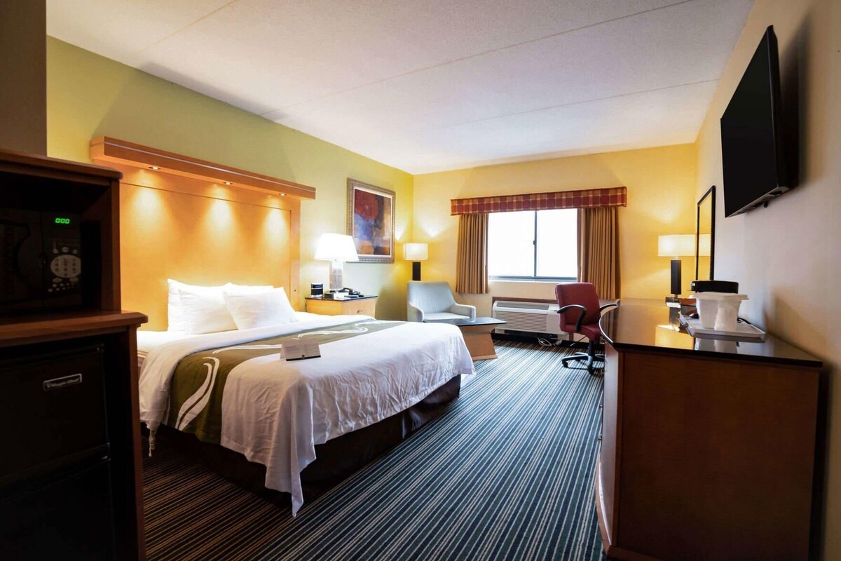 A hotel room with a bed, bedside table, lamp, chair, desk, and a flat-screen TV.